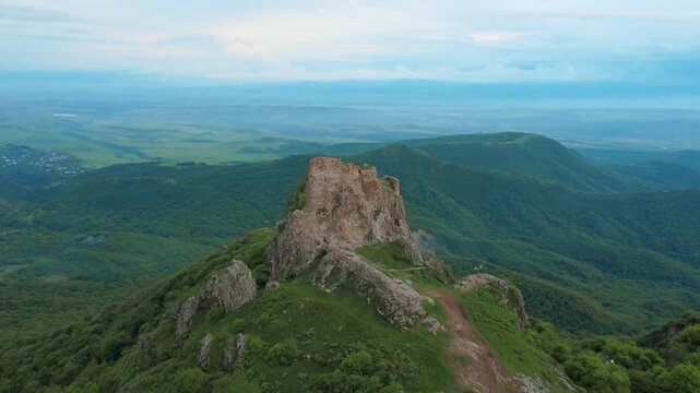 Aerial drone shot slowly flying away from the ancient kojori fortress ruins, also known as azeuli or korogli, perched on a dramatic mountain peak overlooking a vast, lush green valley in georgia