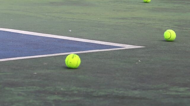 Fluorescent green tennis balls scattered on a hard court surface during a training session for active sports practice