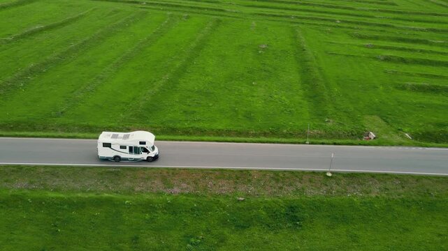 A white camper rides on an empty asphalt road through a vast green landscape with snow-capped mountains in the background, embodying the concept of freedom, travel and adventure vacation in Georgia