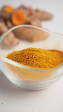 Turmeric powder in glass bowl with fresh root pieces on white background video footage showing close up detail