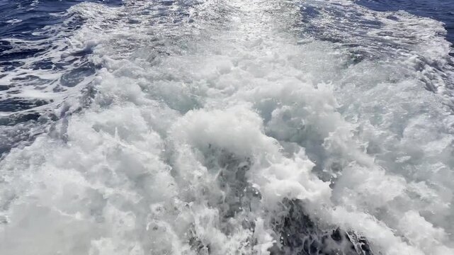 4K stern footage: motorboat propellers churn blue Mediterranean sea into thick white foamy wake. Sunlight glitters on bubbles. Ungraded original background for nautical projects.