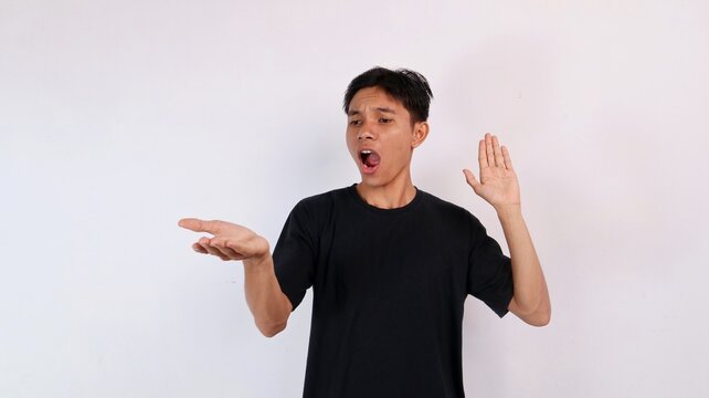 Young Asian man looking at his outstretched palm in utter surprise and astonishment with mouth open against a plain white background.