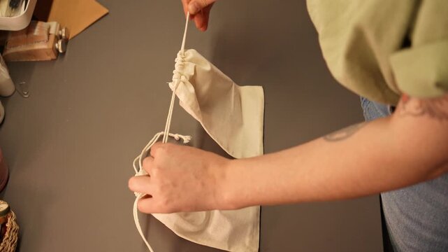 Female artisan places a brown leather wallet into a cotton drawstring pouch. Handmade packaging concept for premium accessories, retail, gifting and small business