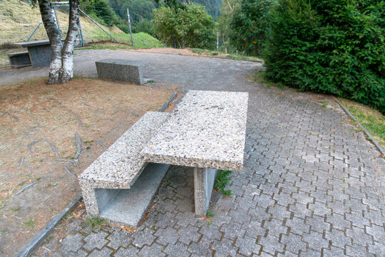 Heavy exposed aggregate concrete picnic table with matching benches stands on a paved outdoor recreation area. Durable vandal resistant public furniture represents park infrastructure, rest areas, lan