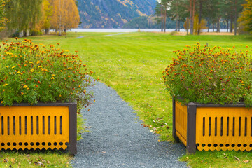 An invitation toward open space leads along a gravel garden path between flowering planters to a broad lawn and distant water in Dalen, Norway, supporting calm outdoor travel and garden themes. © Nimbus Works
