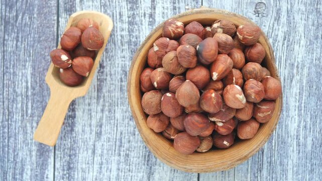 Top view of hazelnuts in wooden bowl and scoop on rustic table surface.