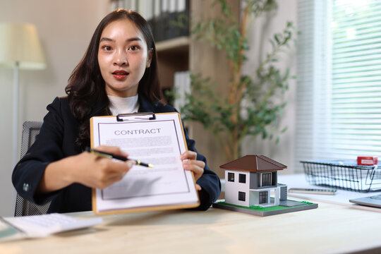 Asian business woman pointing pen at contract document for house purchase.