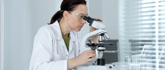 Female scientist working in a modern research laboratory, diligently examining samples under a...