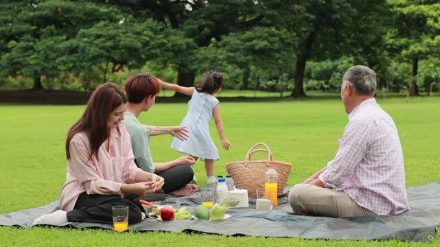 Slow motion hugging Happy father and daughter, Happy Asian family having fun time on picnic at city nature park sunny day, outdoor activitie with daughter father, mother and grandfather