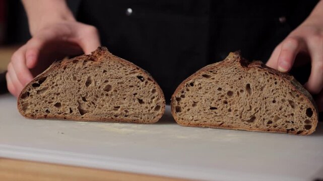 Close up of rustic bread halves on cutting board under warm kitchen light, hands holding loaf edges, showing rugged crust and airy crumb in artisanal bake prep scene