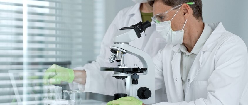 Scientific team analyzing samples in a modern laboratory, focusing on research and development for health care solutions, using advanced microscopes and digital data for discovery and progress