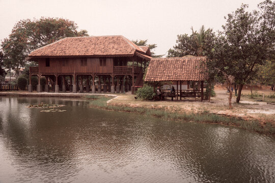 Traditional Betawi Pesisir house with a raised wooden structure, tiled roof, veranda, and pond in Jakarta, Indonesia.