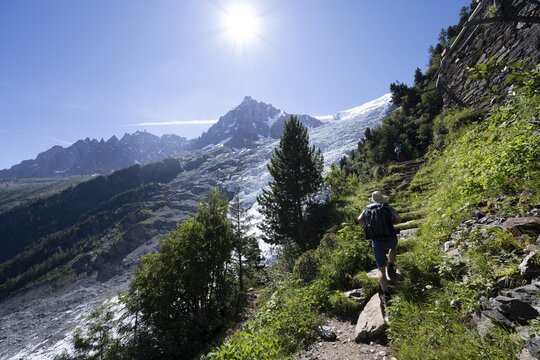 Hiker on hiking trail La Jonction, view of glacier Glacier des Bossons with sun star, behind summit of Aiguille du Midi, Chamonix, Haute-Savoie, France