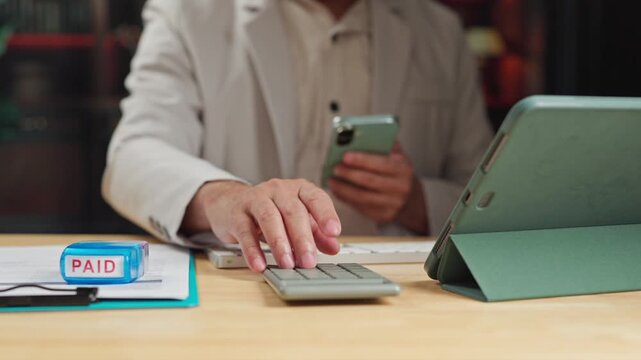 Accountant manages accounting records beside paid invoice stamp, performing online accounting calculation tasks tax review beside calculator.