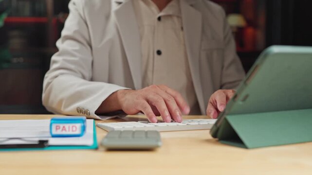 Accountant conducts payment audit procedures, verifying paid invoice documentation before confirming electronic payment approval on tablet.