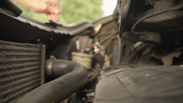 Inside view under car hood: driver opening vehicle bonnet and setting holding prop rod to inspect engine during roadside breakdown repair.