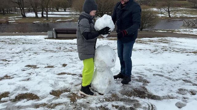 The video captures a father-son duo in their element, laughing as they decorate their snowman and then diving into a spirited snowball fight in the park.
