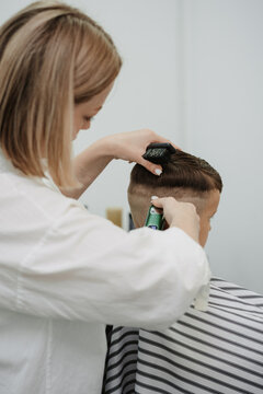 A female hairdresser cuts the back of a little boy's head with a clipper. A professional hairdresser and a child client in a modern barbershop.