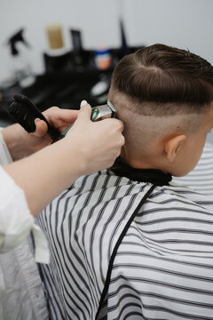 A female hairdresser cuts the back of a little boy's head with a clipper. A professional hairdresser and a child client in a modern barbershop.