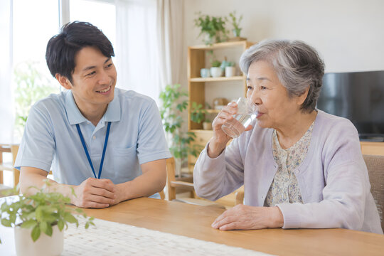 Elderly Japanese woman drinking water with a male caregiver at home