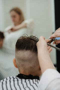 A female hairdresser cuts a little boy's hair with a comb and scissors. A professional hairdresser and a child client in a modern barbershop.
