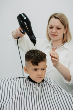 Female hairdresser's hands do a hairstyle for a little boy with a hair dryer, close-up.