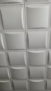 Close up of white plastic polystyrene ceiling tiles texture moving smoothly upward, showing geometric pattern and worn surface for home renovation, cheap interior remodeling, and DIY repair b-roll.