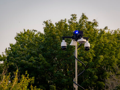 Modern surveillance cameras and security equipment mounted on a tall pole outdoors against trees