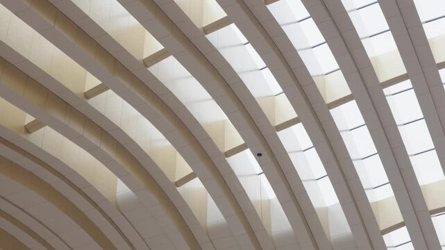 Abstract architectural view of a modern interior ceiling featuring sweeping curved panels, geometric patterns, and large skylights allowing natural light into the building.