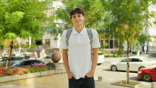 Smiling teenage student wearing a backpack standing outdoors in the city.