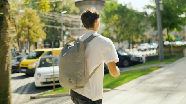 Active male learner wearing a backpack running away in the sunny park.