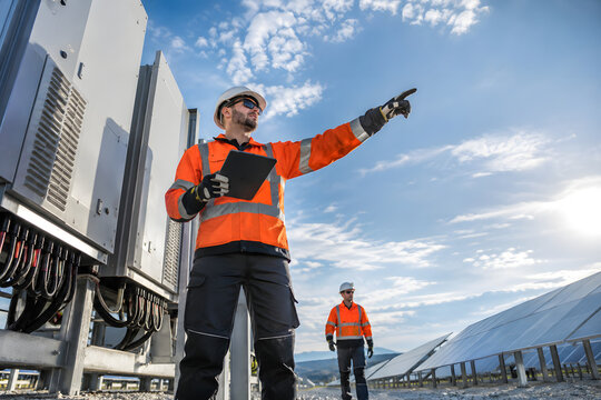 Solar technicians discussing field maintenance from a dramatic ground-level viewpoint.