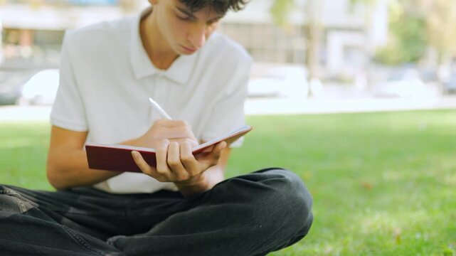 Caucasian young scholar writing notes during an outdoor campus study session.