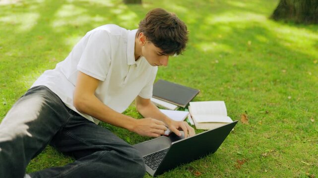 Dedicated young scholar studying with a laptop and notebook on the lawn.