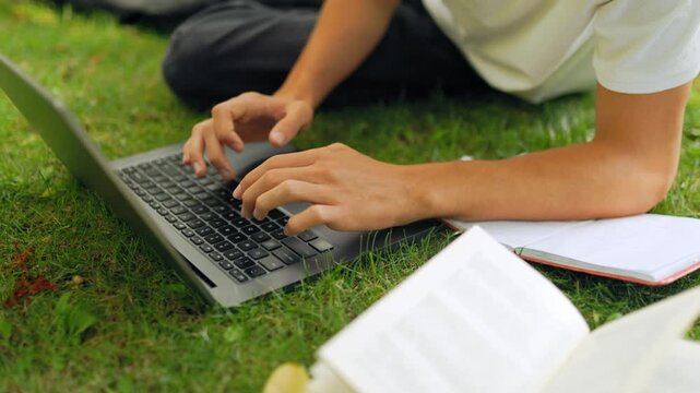 Close up view of student hands typing on a laptop keyboard outdoors.