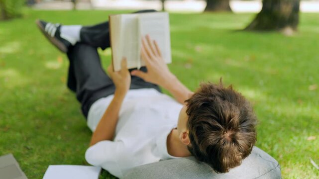 Close up view of a focused guy reading educational literature on the lawn.