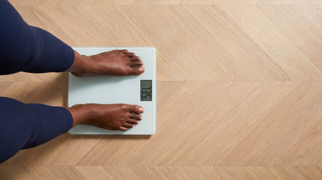Top view of bare feet on digital scale on herringbone wood floor
