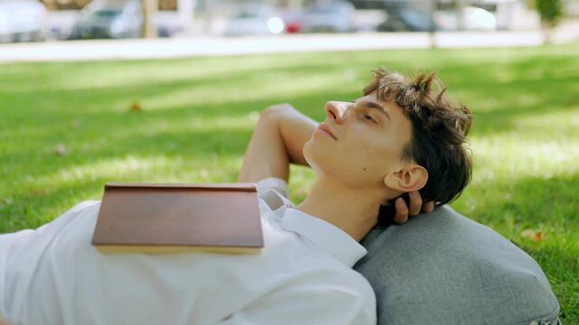 Thoughtful caucasian scholar looking away while resting on the outdoor lawn.