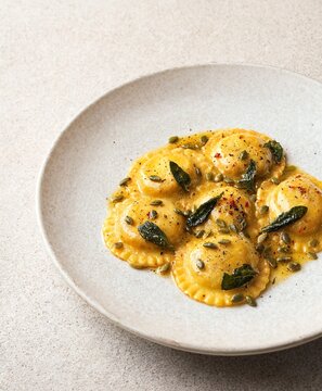 Fresh pumpkin ravioli pasta topped with crispy sage leaves and roasted pumpkin seeds on a ceramic plate
