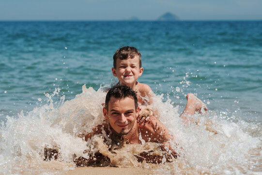 A happy father and son are lying on the sand.