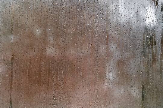 Glass with dense condensation forms abstract backdrop featuring wet texture and diffused light. Surface symbolizes climate, rainfall, humidity, melancholy mood and environmental concept.