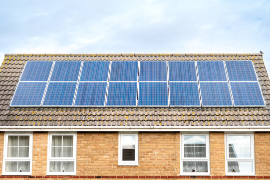 Residential brick house with a large array of solar panels installed across the tiled roof under a bright sky