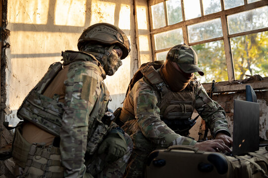 Soldiers operate a drone control console. Military personnel are carrying out a combat mission at a position in an abandoned house.