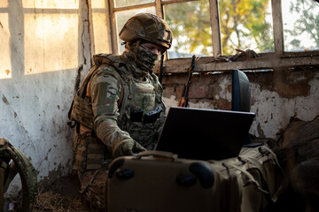 Obraz premium Soldier operates a drone control console. Military personnel is carrying out a combat mission at a position in an abandoned house.