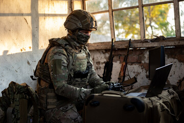 Obraz premium Soldier operates a drone control console. Military personnel is carrying out a combat mission at a position in an abandoned house.