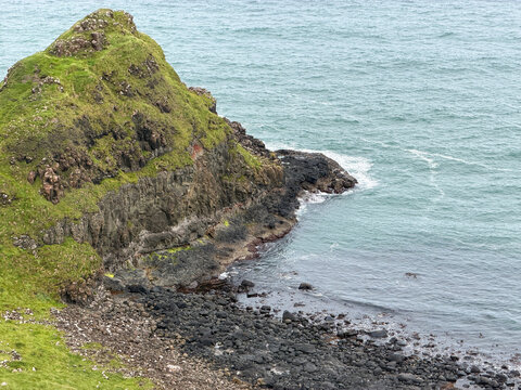 Steep green cliffs descend to dark basalt rocks and Atlantic waters along the rugged Causeway Coast in County Antrim, Northern Ireland.