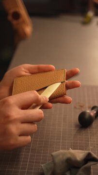 Female artisan shapes and smooths a leather wallet pocket with a bone folder. Leathercraft finishing for handmade accessories, premium goods and small business