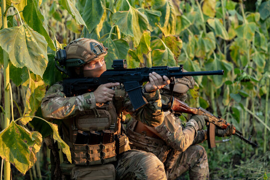 Military Soldiers with assault rifles at a combat position in a field. Military personnel carrying out a combat mission.