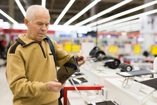 elderly man examines tablet computer in showroom of electronics store