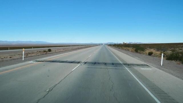 Pov shot driving on straight empty two lane highway through an arid desert landscape. Capturing the essence of an american road trip and endless travel. Car travel or transportation of cargo and goods